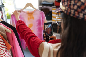 Mulher fotografa uma camiseta tie-dye em um cabide, representando o uso de aplicativo de desapego para compartilhar e vender roupas usadas